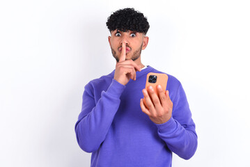 young arab man with curly hair wearing purple sweatshirt over white background holding modern...