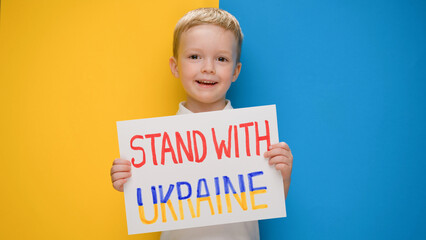 Portrait happy smiling little boy calls to Stand with Ukraine, raises banner with inscription stop war in Ukraine standing on blue-yellow studio background. No war, stop war, russian aggression.