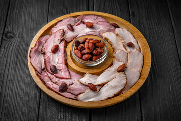 Thinly sliced lard and bacon with roasted almonds and nuts. Snack for Oktoberfest beer or vodka. Wooden plate on black boards.