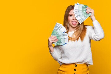 Playful girl in white sweater poses with two fans of 100 euro cash. Young Woman holding paper...