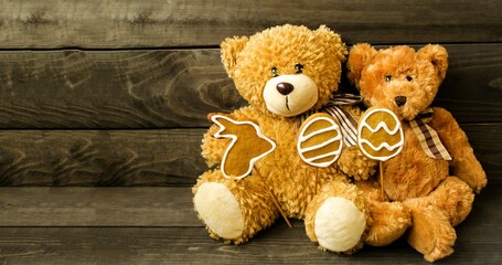 Banner on a wooden background brown fluffy teddy bears sit in paws with Easter cookies, a rabbit and eggs.  Holiday atmosphere.  Copy space for text, decorative postcard.