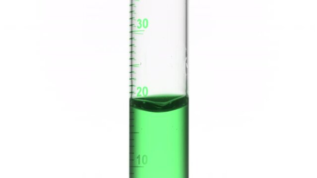 Drop of green fluid is falling down into graduated cylinder with green transparent fluid on white background | Abstract face care cosmetics formulation concept