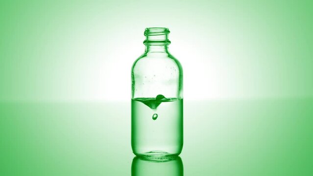 Drop of citric acid falls down into medical bottle with green transparent liquid on green background | Abstract body care cosmetics with citric acid formulating concept