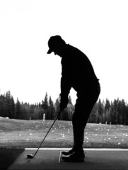 Silhouette of a man holding his driver as he practices his golf swing at a driving range facility...