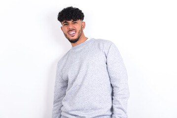 young arab man with curly hair wearing sport sweatshirt
over white background winking looking at...