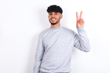 Fototapeta premium young arab man with curly hair wearing sport sweatshirt over white background showing and pointing up with fingers number two while smiling confident and happy.