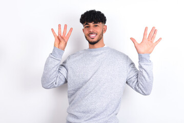 Fototapeta premium young arab man with curly hair wearing sport sweatshirt over white background showing and pointing up with fingers number nine while smiling confident and happy.
