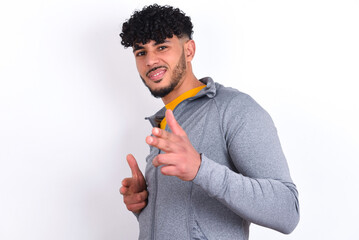 Joyful young arab man with curly hair wearing sport clothes over white background wink and points...