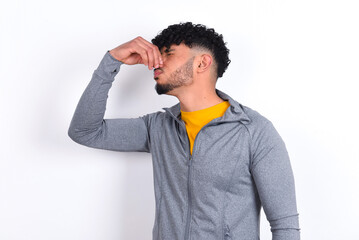young arab man with curly hair wearing sport clothes over white background smelling something...