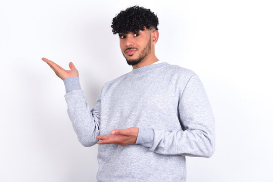 young arab man with curly hair wearing sport sweatshirt
over white background pointing aside with both hands showing something strange and saying: I don't know what is this. Advertisement concept.