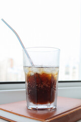 A glass of cola with ice is on the windowsill, a summer drink that saves from the heat