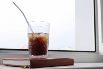 Close-up of a woman's hand holding an ice cola in a glass. Food and drink concept. Addiction to carbonated drinks. Red nails, manicure style