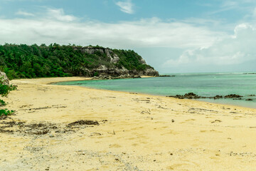 Linda praia com algumas pedras, pessoas tomando banho, montanhas com mata verde ao redor e paisagem marítima ao fundo com ondas e nuvens, localizada na Praia dos Espelhos, Bahia.