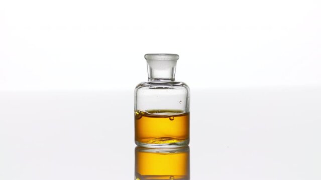 Drop of argan oil falls down into clear old fashioned bottle with yellow transparent liquid on white background | Abstract body care cosmetics with argan oil formulation concept