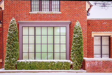 Fototapeta na wymiar Large multi-paned window framed by hedge and tall evergreens to either side in modern home on snowy day