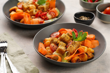 Sweet potato gnocchi with teriyaki tofu with indonesian vegetable salad gado gado - carrots, cucumbers, tomatoes, coriander, sesame seeds and peanut butter dressing in a grey bowl