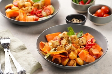 Sweet potato gnocchi with teriyaki tofu with indonesian vegetable salad gado gado - carrots, cucumbers, tomatoes, coriander, sesame seeds and peanut butter dressing in a grey bowl