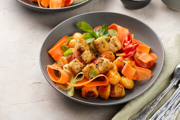 Sweet potato gnocchi with teriyaki tofu with indonesian vegetable salad gado gado - carrots, cucumbers, tomatoes, coriander, sesame seeds and peanut butter dressing in a grey bowl