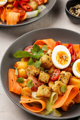 Sweet potato gnocchi with teriyaki tofu with indonesian vegetable salad gado gado - carrots, cucumbers, tomatoes, coriander, sesame seeds, boiled eggs and peanut butter dressing in a grey bowl