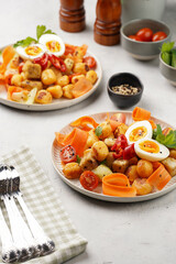 Sweet potato gnocchi with teriyaki tofu with indonesian vegetable salad gado gado - carrots, cucumbers, tomatoes, coriander, sesame seeds, boiled eggs and peanut butter dressing on a white plate