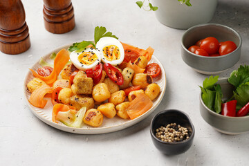 Sweet potato gnocchi with teriyaki tofu with indonesian vegetable salad gado gado - carrots, cucumbers, tomatoes, coriander, sesame seeds, boiled eggs and peanut butter dressing on a white plate