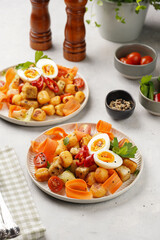 Sweet potato gnocchi with teriyaki tofu with indonesian vegetable salad gado gado - carrots, cucumbers, tomatoes, coriander, sesame seeds, boiled eggs and peanut butter dressing on a white plate