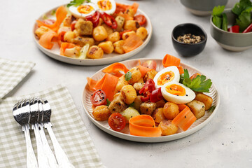 Sweet potato gnocchi with teriyaki tofu with indonesian vegetable salad gado gado - carrots, cucumbers, tomatoes, coriander, sesame seeds, boiled eggs and peanut butter dressing on a white plate