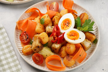 Sweet potato gnocchi with teriyaki tofu with indonesian vegetable salad gado gado - carrots, cucumbers, tomatoes, coriander, sesame seeds, boiled eggs and peanut butter dressing on a white plate