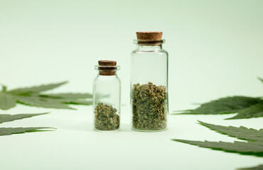 ground marijuana in glass bottles with cork stopper and green leaves, green background.