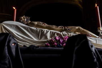 Photograph of jesus lying on his deathbed in a holy week procession in spain. Unrecognizable Nazarenes with a mask on their face carry on their shoulders the body of the dead Christ.