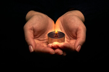 Close-up of hands holding a burning candle in the dark. Adult woman with a candle in her hands on a...