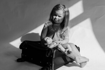 Miserable girl, little sad depressed girl holding her toy and begging for help while feeling unhappy, sitting on suitcase.