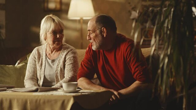 Irritated aged husband blaming upset wife while sitting on sofa at home together