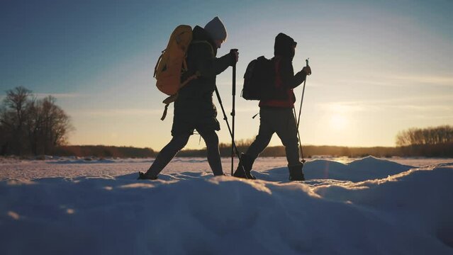 nordic walking in winter. winter hike group of tourists silhouette. teamwork travel. two hikers with sticks walk in the winter sunset in the snow at silhouette. activities in winter happy family