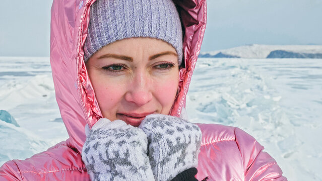 Girl walking on cracked ice of frozen lake Baikal. Woman traveler explores and looks at an ice floe. Magic purest place in nature. Ice arounds traveler all his trip. Hiker walk in cosmic pink jacket.