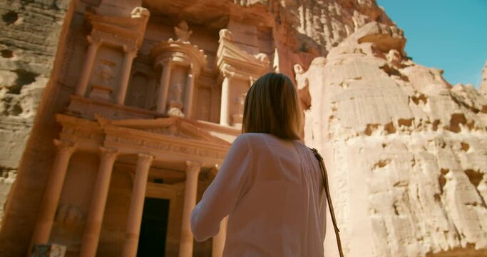 Female traveler takes picture of Petra temple - Treasury Al-Khazneh carved out of rock face in ancient city. Most popular tourist attraction in Jordan, Middle East. 4K medium gimbal shot