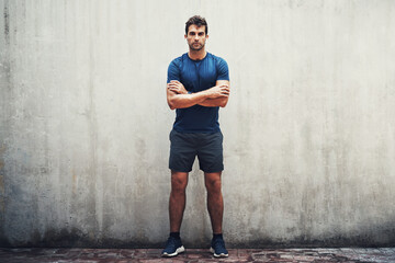 No challenge will ever stand in my way. Portrait of a sporty young man standing against a grey wall while exercising outdoors. - Powered by Adobe