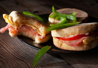 Breakfast egg and ham english muffins with tomato cheese and mayo, with slices of green peppers, dark food photography
