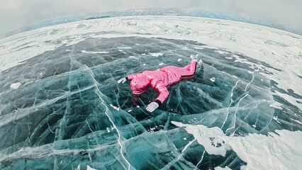 Girl walking on cracked ice of frozen lake Baikal. Woman traveler explores and looks at an ice floe. Magic purest place in nature. Ice arounds traveler all his trip. Hiker walk in cosmic pink jacket.