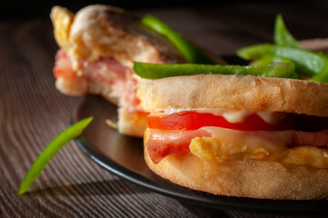 Breakfast egg and ham english muffins with tomato cheese and mayo, with slices of green peppers, dark food macrophotography
