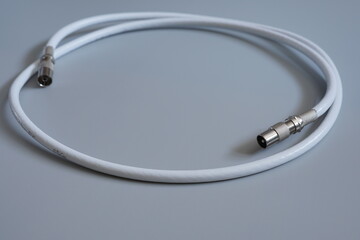 The coaxial cable with professional connectors is rolled up in a ring on a gray background.