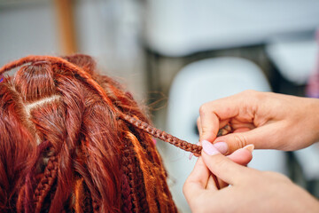 Braiding process plait with colored kanekalon. Beauty salon services. Girl hairdresser weaves woman...