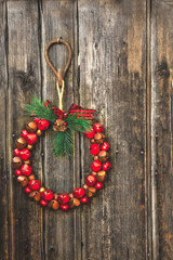 A Christmas wreath of red and brown bells hanging from a rustic hook on a wood plank wall