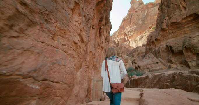 Tourist woman visits Petra taking photo of ancient Red Rode City. Girl hikes in gorge and rock canyon with camera. Most popular attraction in Jordan, Middle East. 4K tracking gimbal medium shot