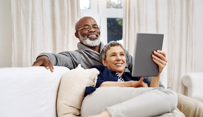 Spending the day together at home. Shot of an affectionate senior couple using a tablet while relaxing on the sofa at home. - obrazy, fototapety, plakaty