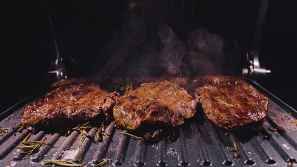 Delicious juicy meat steak cooking on grill. Aged prime rare roast grilling tenderloin fresh marble tenderness beef. Prime beef fry on electric roaster, rosemary, black pepper, salt. Slow motion.