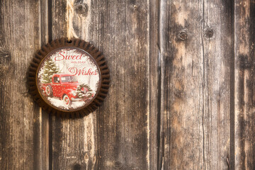 A vintage Christmas ornament made of steel with a truck on it hanging by twine from a weathered wood plank wall