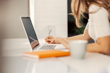 The woman writes down on paper and works from home on the laptop.