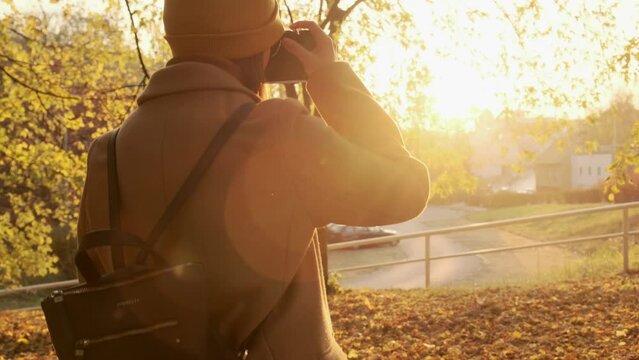 A woman photographer raises the camera to take a picture of the autumn forest at sunset.