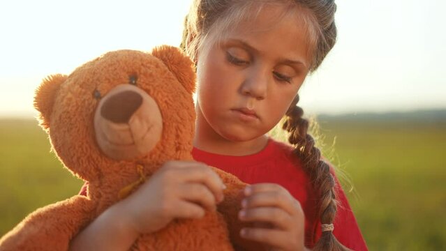 sad girl holding a teddy bear. family violence orphanage concept. upset girl with teddy bear in the park in nature. autistic orphan child with a toy in his hands sunlight